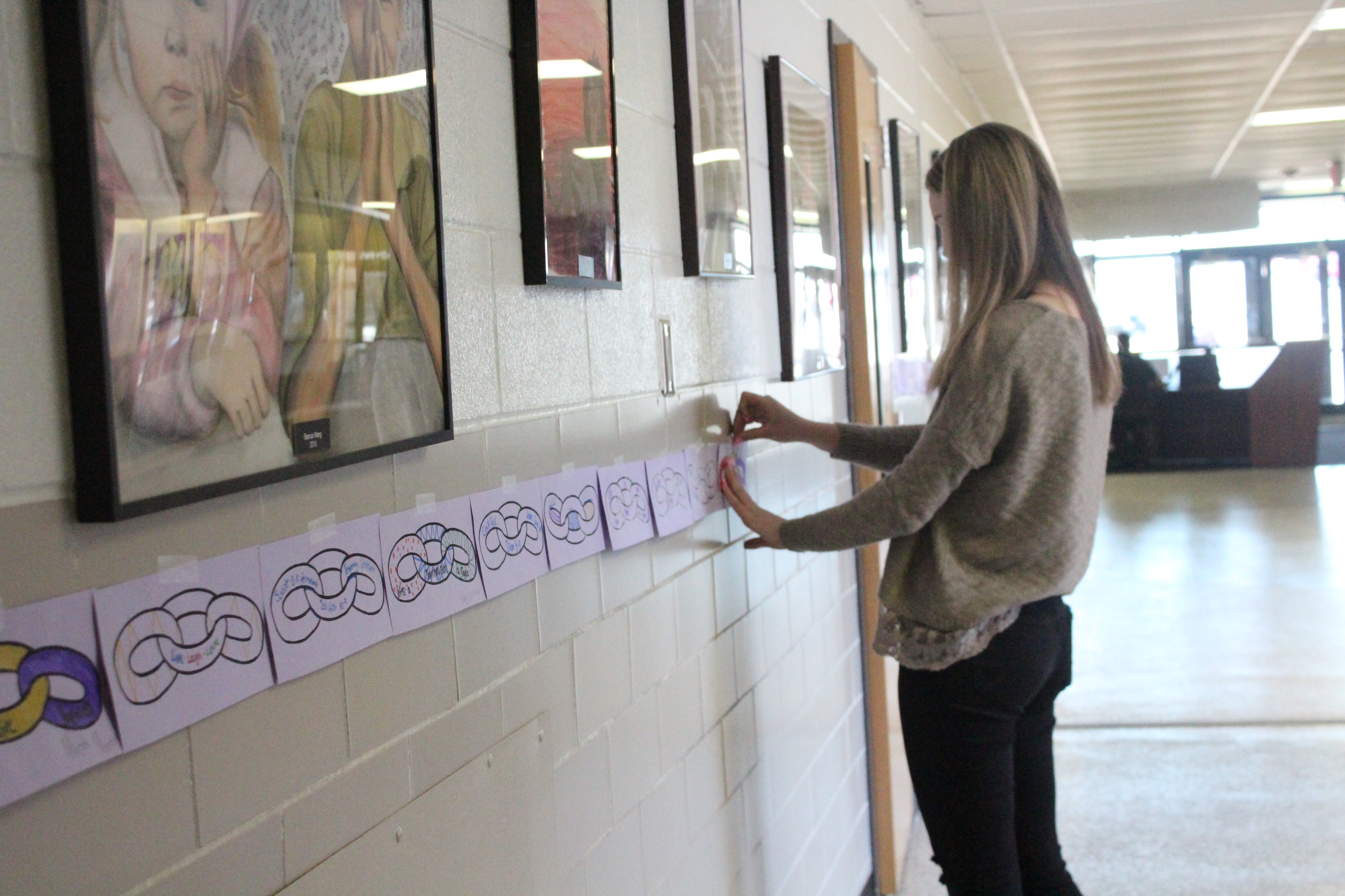 A teacher taping up links in the hallway.